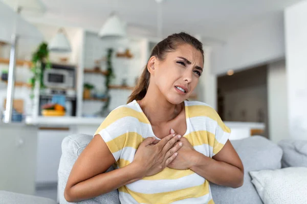 痛みを感じ 胸に触れる若い女性は心臓発作を起こしながら自宅で心臓病に苦しんでいます — ストック写真