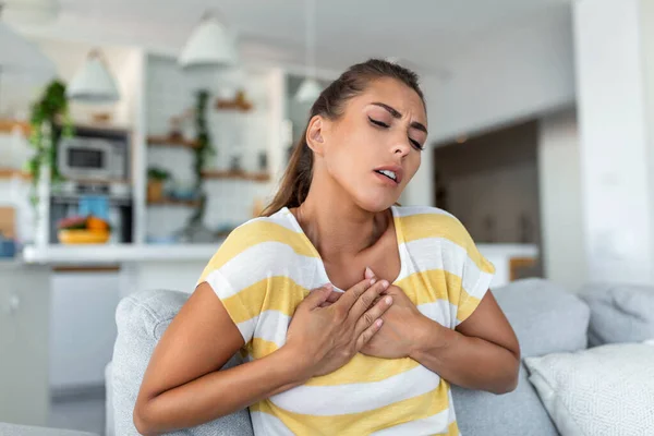 Stressed young woman feeling pain and touching chest suffer from heartache disease at home while having heart attack, infarction