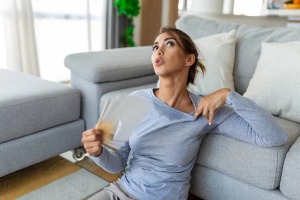 压力大 烦躁的女人挥动风扇就会出现过热 夏季热量降激素问题 家里没有空调坐在沙发上感觉筋疲力尽 中暑的概念 — 图库照片