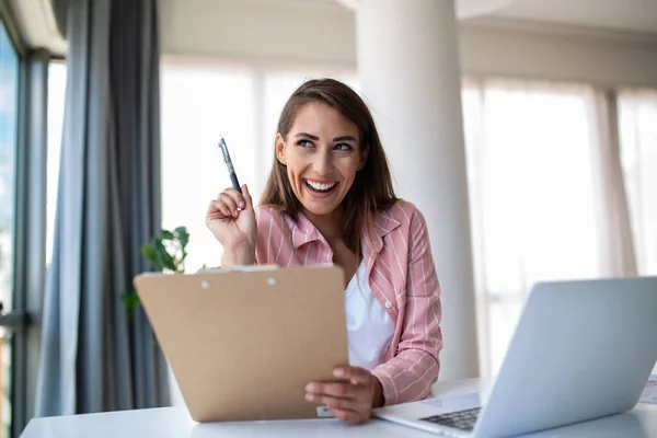 Remote job, technology and people concept - happy smiling young business woman with laptop computer and papers working at home office