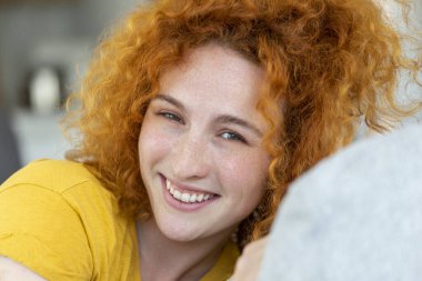 Evdeki kanepede oturan ve kameraya bakan mutlu genç kadın. Yaz boyunca gülümseyen ve rahatlatan güzel bir kadının portresi..