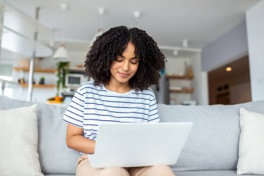 Çekici genç bir kadın evdeki kanepesinde tek başına oturuyor ve bilgisayarını kullanıyor.