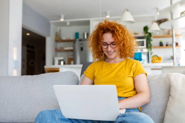 Woman sitting with computer on sofa, studying at home, e-learning and remote freelance job concept