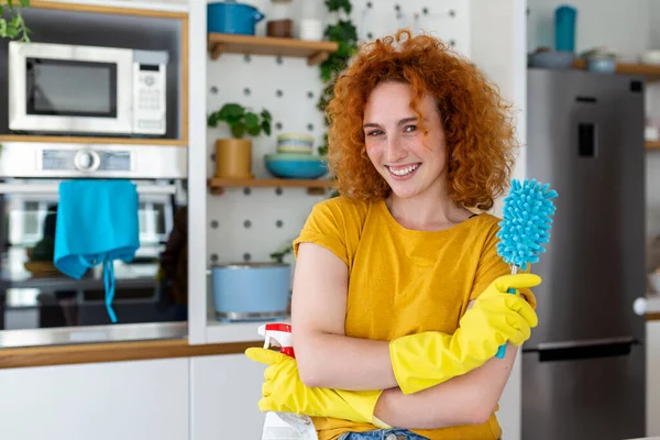 Young woman doing house chores holding cleaning tools. Woman wearing rubber protective yellow gloves, holding rag and spray bottle detergent. It's never too late to clean