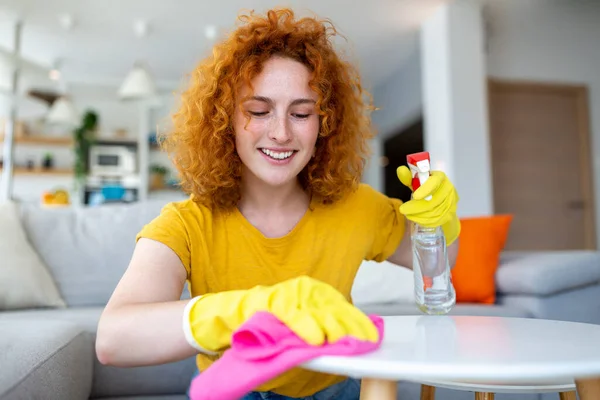 Beautiful young woman cleaning the house. Girl rubs dust. Smiling woman wearing rubber protective yellow gloves cleaning with rag and spray bottle detergent. Home, housekeeping concept.
