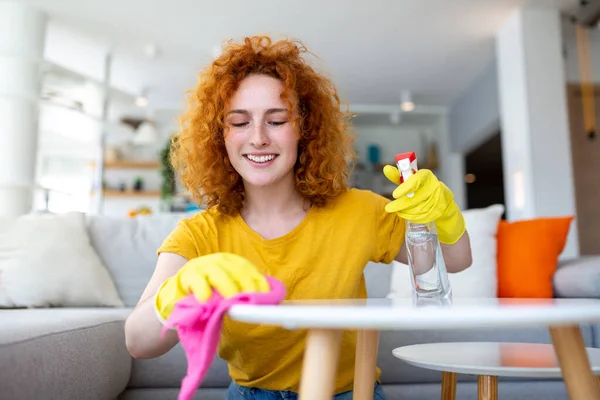 Beautiful young woman cleaning the house. Girl rubs dust. Smiling woman wearing rubber protective yellow gloves cleaning with rag and spray bottle detergent. Home, housekeeping concept.
