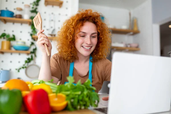 若い女性が料理を学ぶ 彼女は台所でラップトップ上のビデオレシピを見て 料理を調理します 家庭料理の概念 — ストック写真