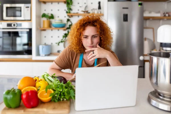 一个年轻的女人学习做饭 她在厨房的笔记本电脑上看视频菜谱 做一道菜 在家做饭的概念 — 图库照片