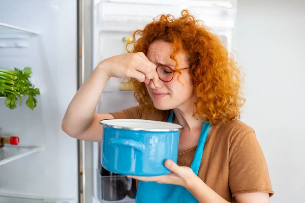 Bad Food In Fridge, young woman in holding her nose because of bad smell from food in refrigerator at home