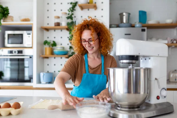 stock image Happy attractive young adult woman housewife baker wear apron holding pin rolling dough on kitchen table baking pastry concept cooking cake biscuit doing bakery making homemade pizza at home