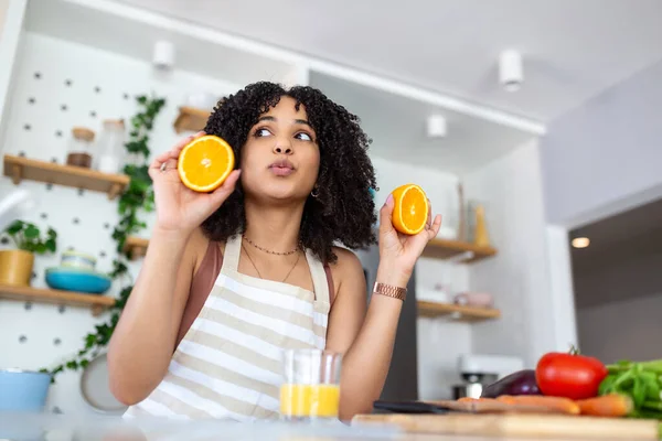 キッチンで新鮮なオレンジジュースを飲む美しい若い女性 健康的な食事 幸せな若いです女性とともにガラスのジュースとオレンジでテーブルでキッチン — ストック写真