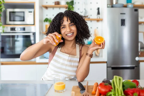 キッチンで新鮮なオレンジジュースを飲む美しい若い女性 健康的な食事 幸せな若いです女性とともにガラスのジュースとオレンジでテーブルでキッチン — ストック写真