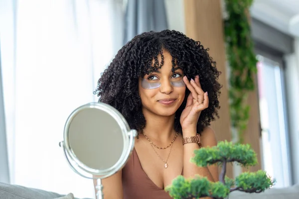Modern cosmetology and patches against fatigue under the eyes. Cheerful young african american woman applying them under her eyes.