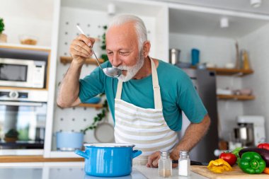 Mutfakta yemek pişiren son sınıf öğrencisi mutlu. Emeklilik, hobi kavramı. Yemek yemek için kaşık tutan gülümseyen son sınıf öğrencisinin portresi.