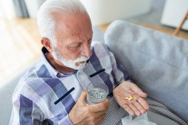 Evdeki kanepede otururken haplar alan kıdemli bir adam, elinde beyaz kavanozla tedavi görüyor, fotokopi çekiyor. Gri saçlı, vitamin takviyesi yapan yaşlı bir adam. Yaşlılık kavramında sağlıklı yaşam tarzı