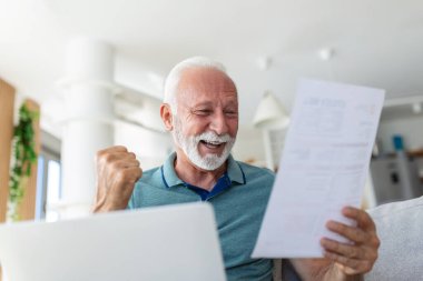 Şaşırtıcı bir şekilde gülen yaşlı, olgun bir adam kağıt dökümanlara bakıyor, finansal bilgileri analiz ederken heyecanlanıyor, vergi iadesi veya evde banka kredisi onayı alıyor..