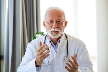 Doktor hatta. Kıdemli sıhhiyeci ofisinden dizüstü bilgisayarla müşteriyle konuşuyor. Yetişkin erkek terapist, konsültasyonda dizüstü bilgisayarla hastaya tıbbi tedaviyi anlatıyor..