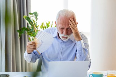 İyi olmayan kıdemli bir iş adamı dizüstü bilgisayarda el pervanesiyle oturuyor. Aşırı ısınmış erkek işçi, ofiste sıcak çarpmasından ve iş yerinde klimasız kalmaktan dolayı bocaladı..