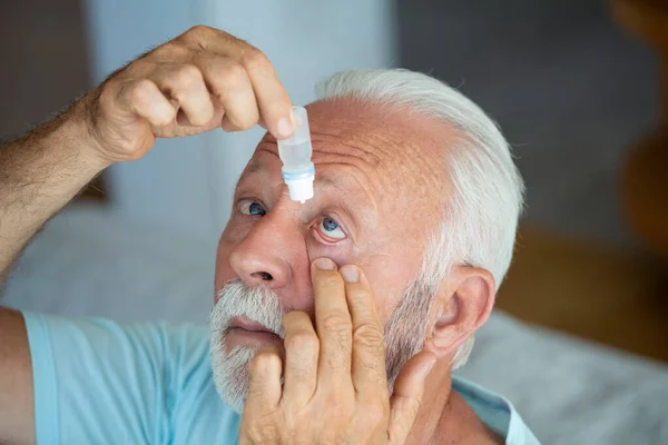 Man putting liquid drops in his eye solving vision problem.Senior dropping eye drop medicine healing his eye pain. Vision and ophthalmology medicine, Senior gray hair man applying eye drop.
