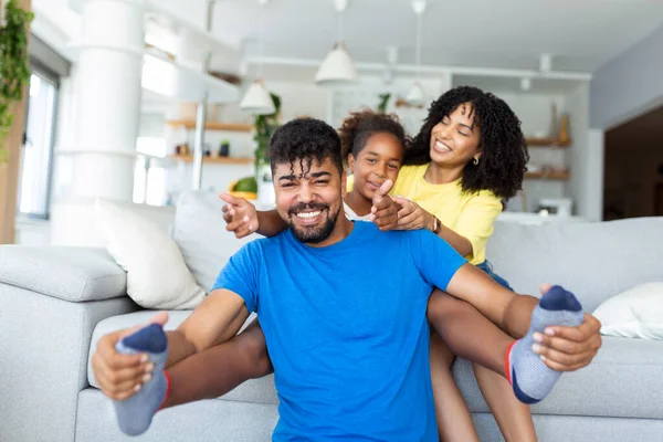 Happy African American dad and mom with excited proud daughter kid, playing flying superhero, reaching arm forward. Cheerful girl playing active game with family at home