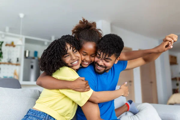 Happy African American dad and mom piggybacking excited proud daughter kid, playing flying superhero, reaching arm forward. Cheerful girl riding fathers back playing active game with family at home