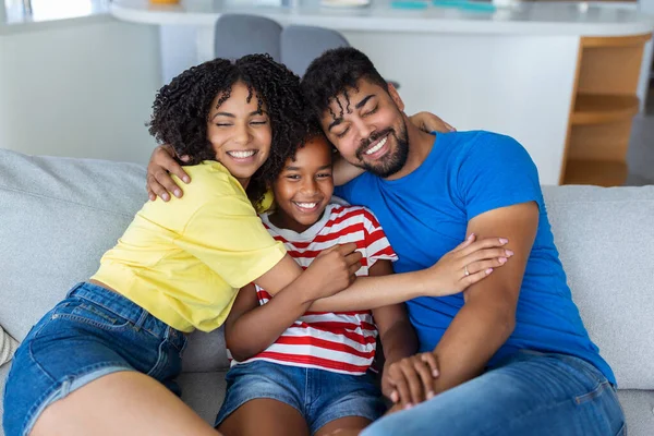 Family picture of smiling young mom and dad sit on couch posing with cute little daughter, small excited funny girl hug happy parents, relax on sofa together