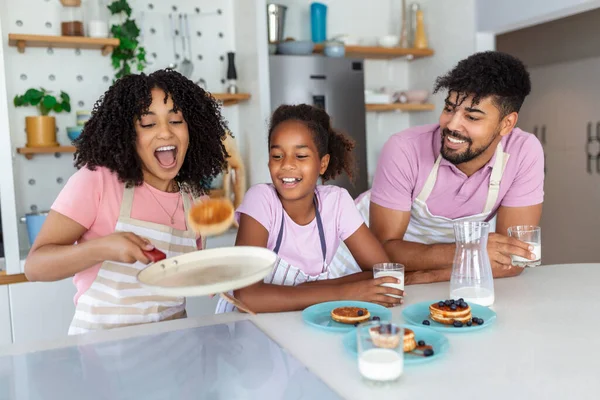 笑顔の母トスパンケーキ彼女は彼女の若い娘にオフに示すように彼らは父と朝食を準備として — ストック写真