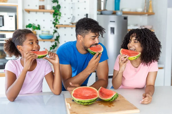 Young Family eating watermelon and having fun. Mixed race family in kitchen together eating a watermelon slice.