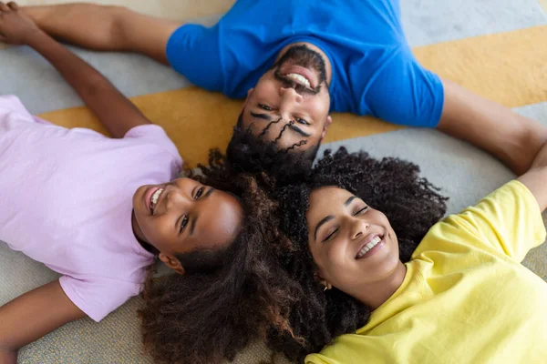 Happy african american family of four bonding lying on bed, black parents and cute little daughter with smiling faces looking at camera in bedroom, mixed race mom dad with child portrait, top view