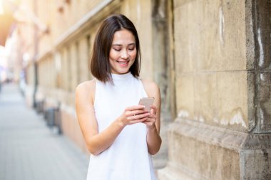 Güzel Asyalı kadın akıllı telefonuyla mesaj göndermek için başvuru formu kullanıyor. Sokakta duran akıllı telefonlu mutlu genç Asyalı kadın.