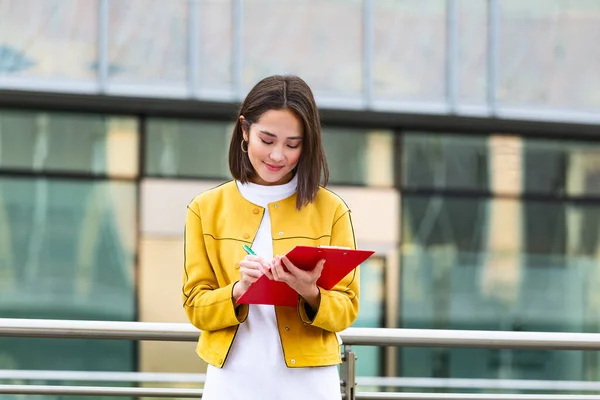 Asian Business woman in casual wear writing on clipboard. business woman holding clipboard. Modern, hardworking woman holding clip board in hands, writing on documents.
