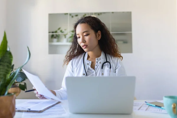 Doctor professional female Asian doctor wearing uniform taking notes in medical journal, filling documents, patient illness history, looking at laptop screen, student watching webinar