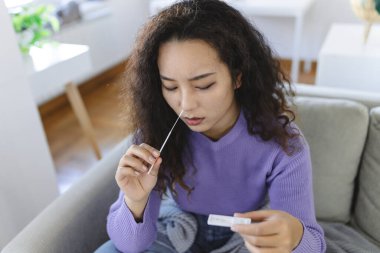 Asian woman using cotton swab while doing coronavirus PCR test. Woman takes coronavirus sample from her nose at home. woman at home using a nasal swab for COVID-19.