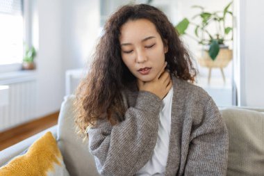 Close up of young Asian woman rubbing her inflamed tonsils, tonsilitis problem, cropped. Woman with thyroid gland problem, touching her neck, girl has a sore throat
