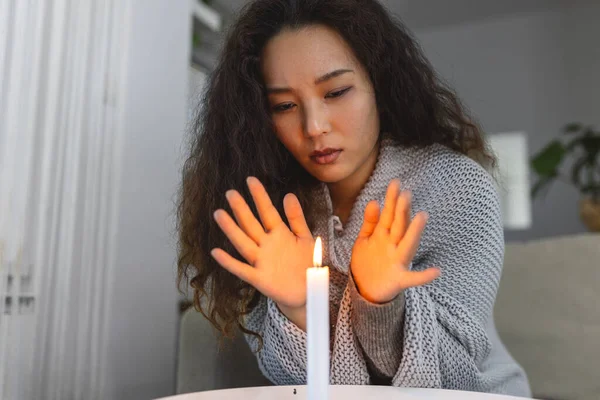 Burning candle, women trying to heat her hands in dark home. Shutdown of heating and electricity, power outage, blackout, load shedding or energy crisis
