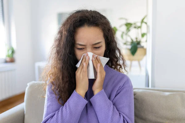 Sick desperate Asian woman has flu. Rhinitis, cold, sickness, allergy concept. Pretty sick woman has runnning nose, rubs nose with handkerchief. Sneezing female. Brunette sneezing in a tissue