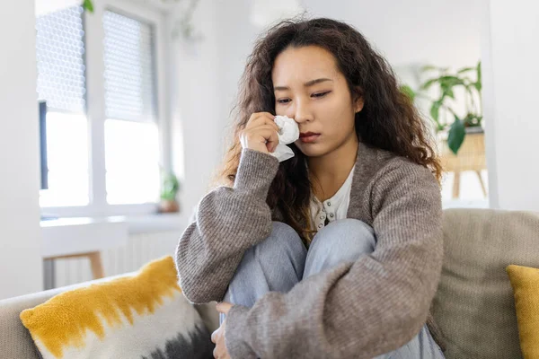 Unhappy young Asian woman crying alone close up, depressed girl sitting on couch at home, health problem or thinking about bad relationships, break up with boyfriend, divorce