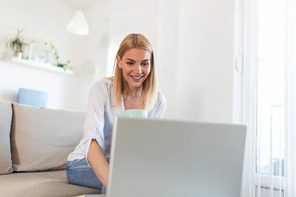Beautiful woman freelancer noting information for planning project doing remote job via laptop computer. Woman smiling while reading email on modern laptop device .