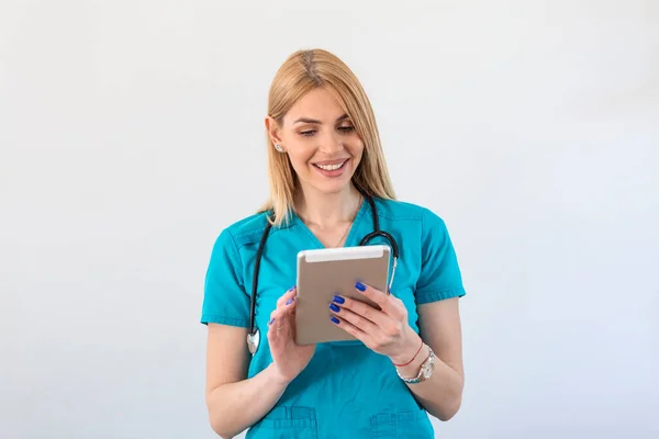 Young female clinician doctor in scrubs using touchpad while communicating with patients online