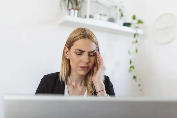 Young frustrated woman working at office desk in front of laptop suffering from chronic daily headaches. Feeling exhausted. Frustrated young woman looking exhausted while sitting at her working place