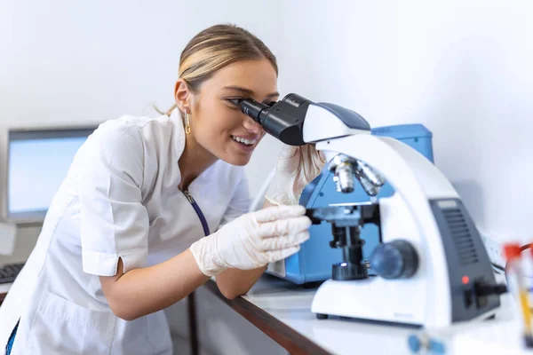 Scientist in Glasses Looking a Petri Dish with Genetically Modified Sample Chemicals Under a Microscope. Microbiologist Working in Modern Laboratory with Technological Equipment.