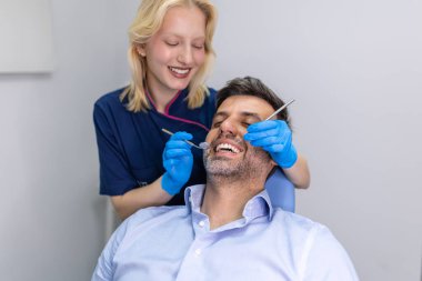 Young female dentist examining teeth of her patient during appointment at dental clinic. Hands of a doctor holding dental instruments near patient's mouth. Healthy teeth and medicine concept clipart
