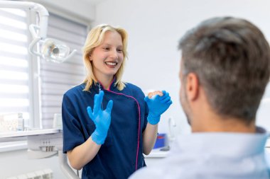 Dentist showing dental plaster mold to the patient. Dentist doctor showing jaw model at dental clinic, dental care concept. Dental care concept. clipart