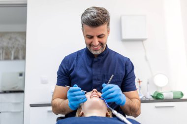 Image of pretty young woman sitting in dental chair at medical center while professional doctor fixing her teeth