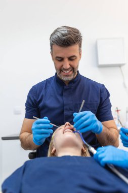Image of pretty young woman sitting in dental chair at medical center while professional doctor fixing her teeth