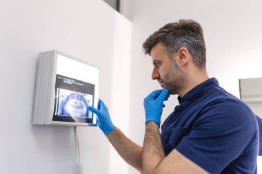 Mavi önlüklü diş hekimi bilgisayar ekranında diş röntgenini inceliyor. Diş hekimleri diş kliniğinde röntgen taraması istiyor..