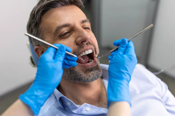 歯科医院で患者の歯を調べる歯科医の肩のビュー 若い女性歯科医に歯を検査された男 — ストック写真