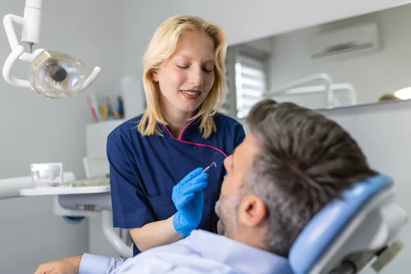 Female dentist curing teeth cavity in blue gloves. Dentist caries treatment at dental clinic office. People, medicine, stomatology and health care concept