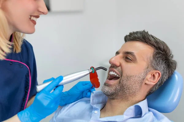 Patient in the dental clinic. Teeth whitening UV lamp with photopolymer composition. Man during teeth whitening procedure with curing UV light at dentist\'s office.