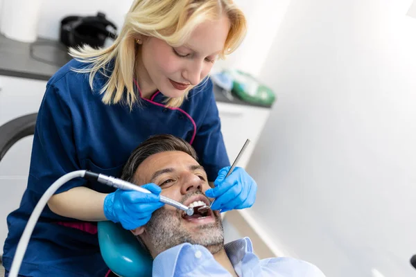 ドリルを保持し 患者の近くに笑みを浮かべて陽気な女性歯科医は 歯科椅子の男性患者に歯を掘削 — ストック写真